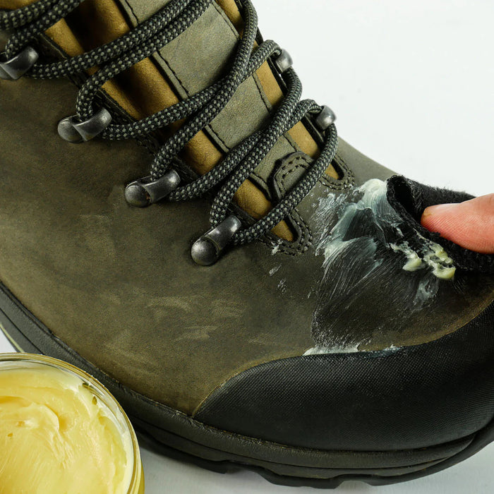 Person applying cream to a green boot with a jar of cream next to it