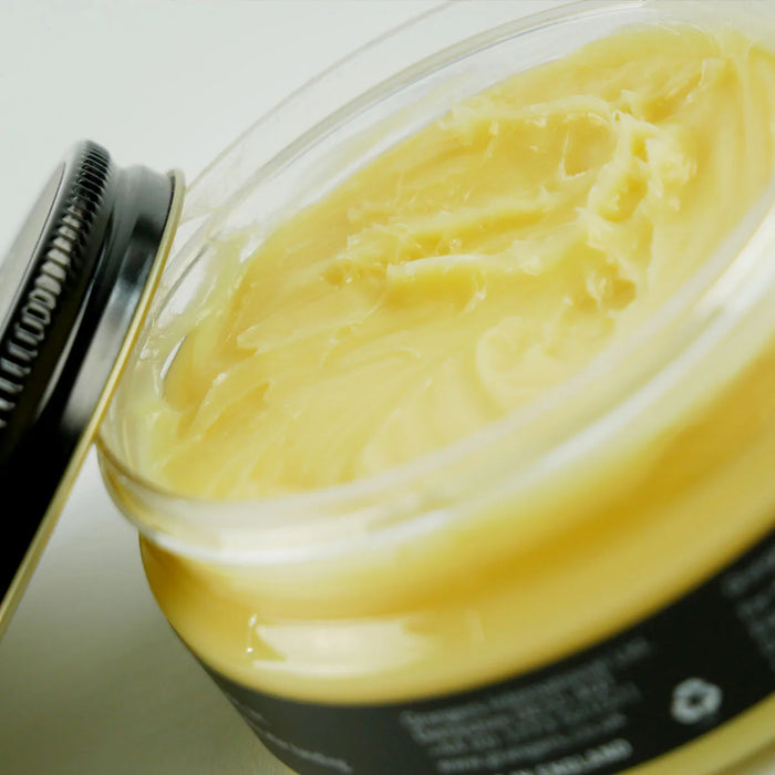 Jar of yellow cream with a black lid on a white background